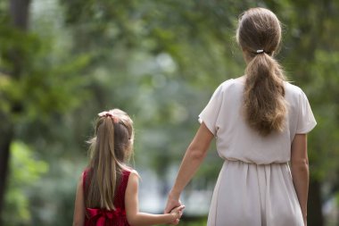 Küçük sarışın uzun saçlı çocuk kız moda elbiseler birlikte bulanık renkli güneşli bokeh arka plan açık havada sıcak güneşli gün tutuşup yürürken ince ince annesi ile arkadan görünüm.