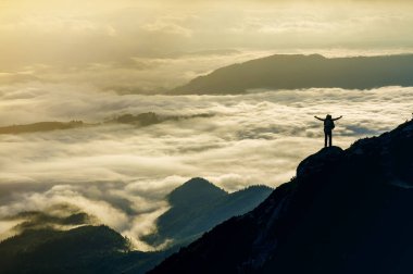 Geniş dağ panorama. Turist ile sırt çantası ile beyaz bulutlar kaplı vadi üzerinden kaldırdı elleriyle kayalık dağ yamacında küçük silüeti. Güzellik, Doğa, turizm ve seyahat kavramı