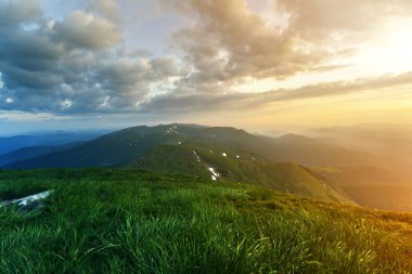 Geniş Yataklı güneş doğarken yaz. Parlayan turuncu güneş mavi bulutlu gökyüzü yeşil çimenli tepe yumuşak çim ve uzak dağ üzerinde yükselterek sabah sis ile kaplı. Doğa kavramının güzellik.