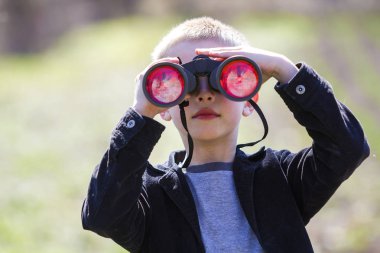 Dikkatle bir şey aracılığıyla dürbün uzaktan izlerken küçük sevimli yakışıklı tatlı sarışın çocuk portresi arka plan bulanık. Çocuk masumiyet, rüyalar, fanteziler ve hayal kavramı.