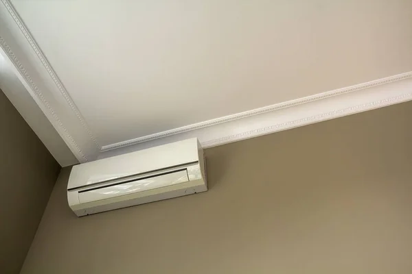 Cool air conditioner installed in room interior on white ceiling and light walls copy space background. Climate control, comfortable home concept.