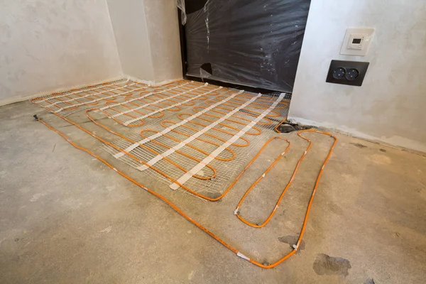 Heating red electrical cable wire system installed on cement floor in small new unfinished room with plastered walls. Renovation and construction, modern technology, comfortable warm home concept.