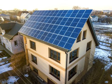 Çatıda mavi parlak güneş enerjili voltaik panelleri olan iki katlı yeni bir yazlık evin havadan görünüşü. Yenilenebilir ekolojik yeşil enerji üretim kavramı.
