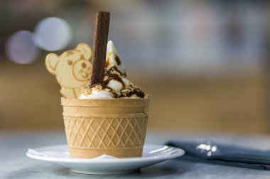 Dondurma Tatlı gofret fincan çikolatalı kurabiye ve yaratıcı dekorasyon Tepesi bulanık renkli iç arka plan üzerinde beyaz plaka.