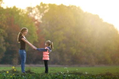Arkadan görünüşü yeşil çayır üzerinde orman ağaçları bulanık arka plan açık havada elele ayakta genç ince çekici anne ve çocuk kız.