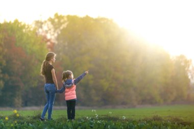 Genç çocuk kız puan gün ışığında yeşil çayır açık havada doğa orman ağaçları zevk çekici anne el holding arka plan bulanık. Mutlu aile ilişkileri kavramı.