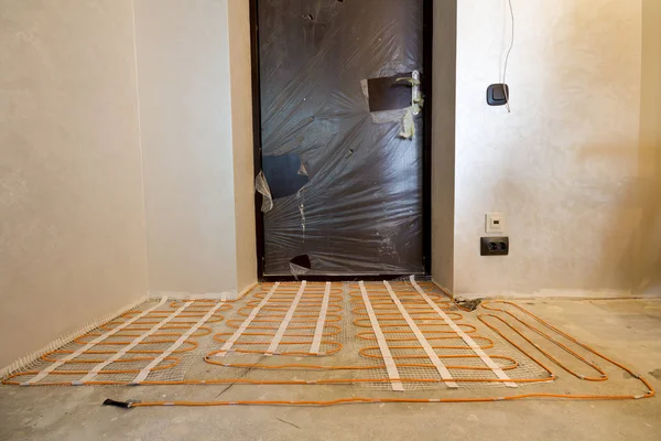 Heating red electrical cable wire system installed on cement floor in small new unfinished room with plastered walls. Renovation and construction, modern technology, comfortable warm home concept.