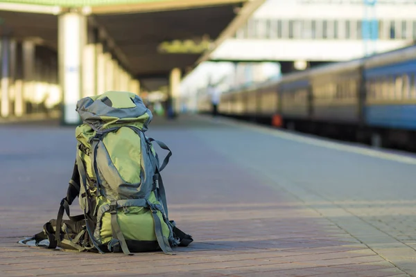 Close-up of big green tourist backpack on railway station platform on blurred background. Traveling, adventure and recreation concept.