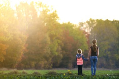 Arkadan görünüşü yeşil çayır üzerinde orman ağaçları bulanık arka plan açık havada elele ayakta genç ince çekici anne ve çocuk kız.