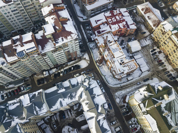 Aerial black and white winter top view of modern city center with tall buildings and parked cars on snowy streets.
