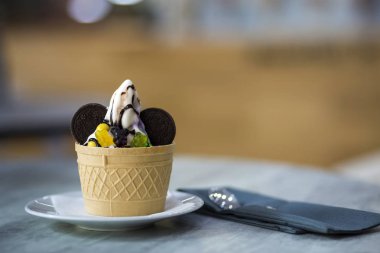 Dondurma Tatlı gofret fincan çikolatalı kurabiye ve yaratıcı dekorasyon Tepesi bulanık renkli iç arka plan üzerinde beyaz plaka.