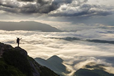 Geniş dağ panorama. Turist ile sırt çantası ile beyaz bulutlar kaplı vadi üzerinden kaldırdı elleriyle kayalık dağ yamacında küçük silüeti. Güzellik, Doğa, turizm ve seyahat kavramı