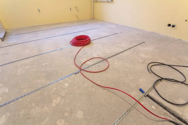 Heating red electrical cable wire installation on cement floor in small new unfinished room with plastered walls. Renovation and construction, comfortable warm home concept.