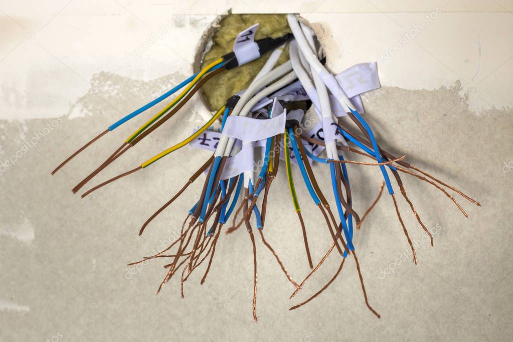 Electrical exposed connected wires protruding from socket on white wall. Electrical wiring installation. Finishing works in renovated apartment.