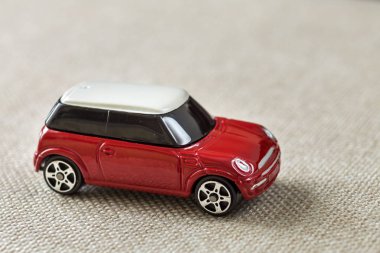 Küçük parlak kırmızı metal basit çocuk oyuncak araba hafif bej tuval bezi kopya alan arka plan üzerinde koyu windows ile.