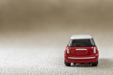 Küçük parlak kırmızı metal basit çocuk oyuncak araba hafif bej tuval bezi kopya alan arka plan üzerinde koyu windows ile.