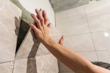 İşçi kiremitçi Close-up yükleme hafif bej seramik karo gelecek banyo duvarları üzerinde eller. Fayans yükleme, ev geliştirme, tadilat ve inşaat, konforlu modern ev concept.