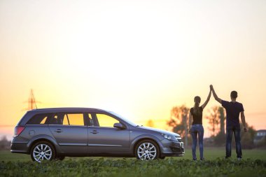 Genç çift, uzun at kuyruğu ve atletik adam tutarak ince çekici kadın yeşil alanında açık gökyüzü günbatımı veya gündoğumu kopya alan arka plan, gümüş renkli araba, silah kaldırdı..