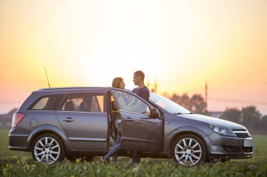 Genç çift, uzun saç ve sportif yakışıklı ince çekici kadın kucakladı birlikte gümüş renkli araba sıcak yaz akşamı üzerinde durabilen parlak gökyüzü günbatımı veya gündoğumu kopya alan arka plan.