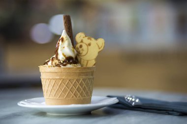 Dondurma Tatlı gofret fincan çikolatalı kurabiye ve yaratıcı dekorasyon Tepesi bulanık renkli iç arka plan üzerinde beyaz plaka.