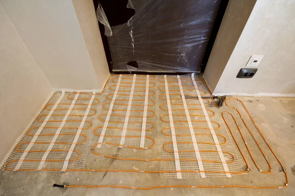 壁を漆喰で小さな新しい未完成の部屋でセメントの床にインストールされている赤い電気ケーブル ワイヤー暖房します。改修や建設、現代のテクノロジー、快適な暖かいホーム コンセプト. — ストック写真