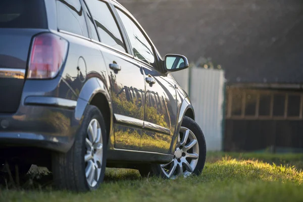 New shiny gray car parked on green grass on blurred sunny summer
