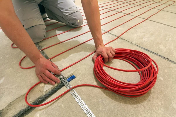 Electrician installing heating red electrical cable wire on ceme
