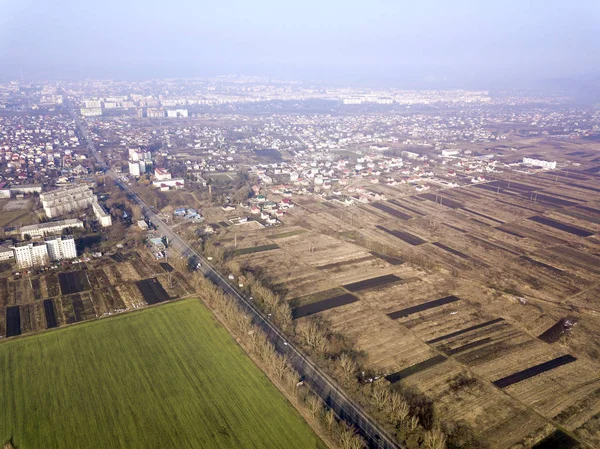 Вид с воздуха на зеленые и вспаханные поля и пригороды города на солнечный — стоковое фото