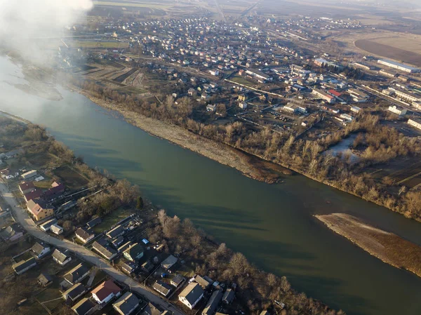Aerial top view of river flowing through town. Rural landscape of residential house roofs, roads and tree tops on spring or autumn day. Drone photography.