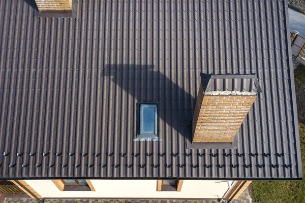 Vista superior aérea de la construcción de techo de tejas empinadas, chimeneas de ladrillo y pequeña ventana del ático en la parte superior de la casa con techo de baldosas de metal. Trabajos de techado, reparación y renovación . — Foto de Stock