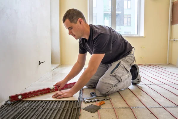 Mladý dělník obkladač instalaci keramických dlaždic pomocí páčky na cemen — Stock fotografie