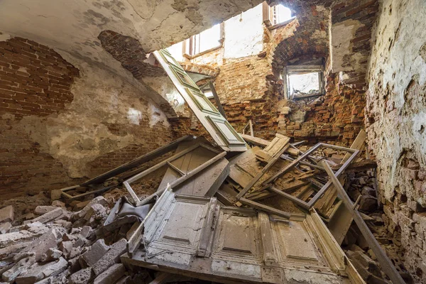 Old forsaken empty basement room of ancient building or palace with cracked plastered brick walls, low ceiling, small windows with and rubbish on dirty floor.