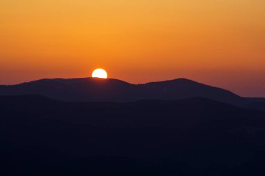 Güzel gün batımı dağlarda. Geniş panorama görüş-in büyük parlak beyaz güneşin karanlık dağ manzara gündoğumu veya günbatımı üzerinde dramatik turuncu gökyüzü altında. Doğa kavramının Güzellik.