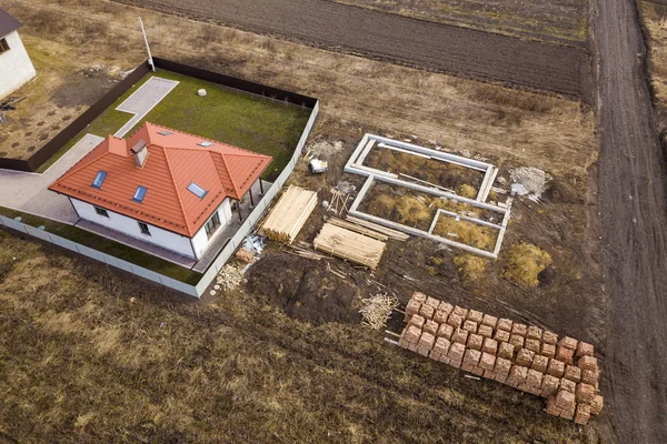 Flyg foto av nya hus tak med vinds fönster och bygg plats, grunden för framtida hus, högar av tegel och bygga timmer stockar för konstruktion. — Stockfoto