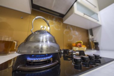 Modern mutfak sarı iç arka plan üzerine kaynar su üzerinde yanan gaz ile parlak paslanmaz çay çaydanlık çaydanlık soba.