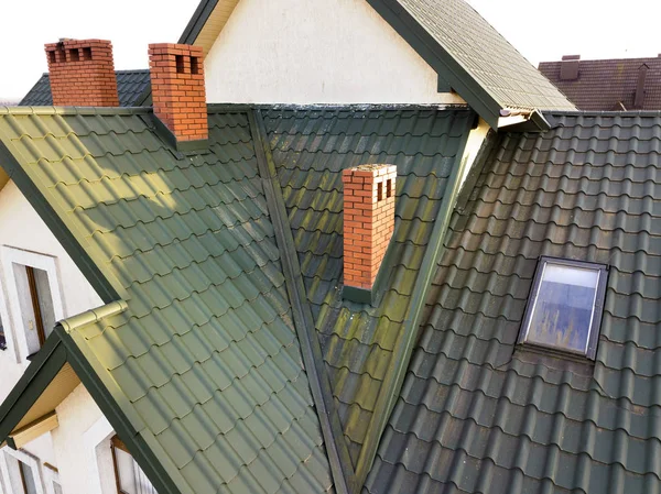 Green metal shingled house roof with attic plastic window and br
