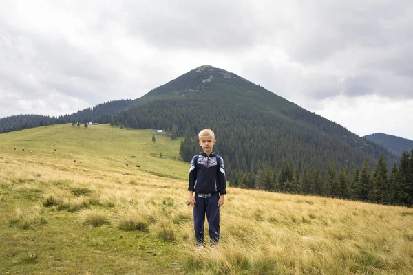 Молодой счастливый улыбающийся мальчик с рюкзаком, стоящим в горах — стоковое фото