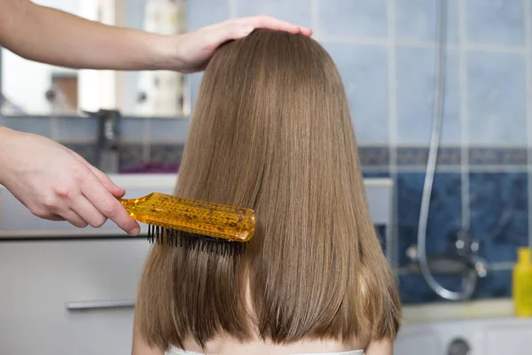 Mano madre con cepillo peinando pelo largo y claro de niña linda —  Fotos de Stock