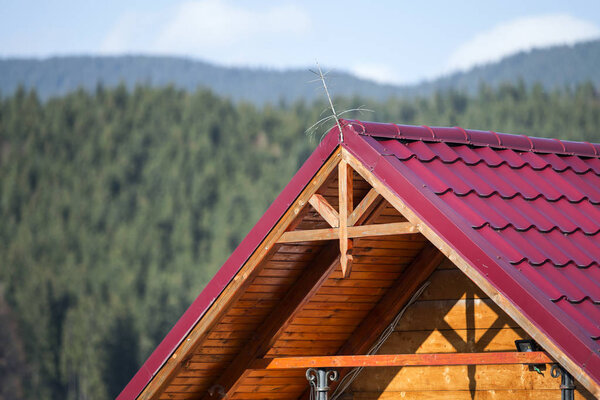 Close-up detail of new modern house top with shingled red roof and wooden sidings on foggy spruce mountains background. Professionally done building and construction work, real estate property.