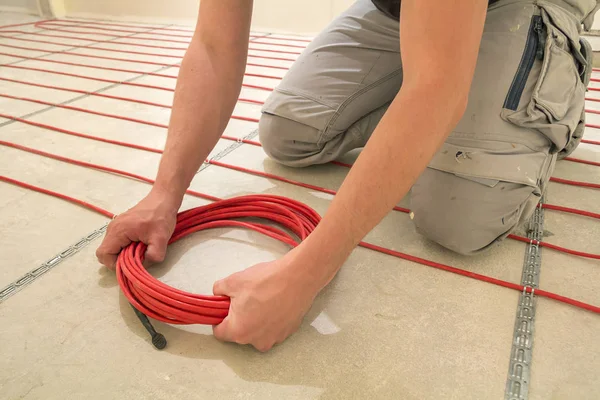 Eletricista instalando aquecimento fio de cabo elétrico vermelho no ceme — Fotografia de Stock