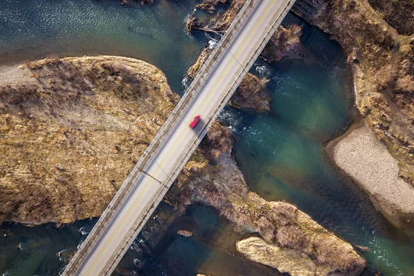 Luchtfoto van witte brug met bewegende rode auto over blauw water en steenachtige eilanden. — Stockfoto