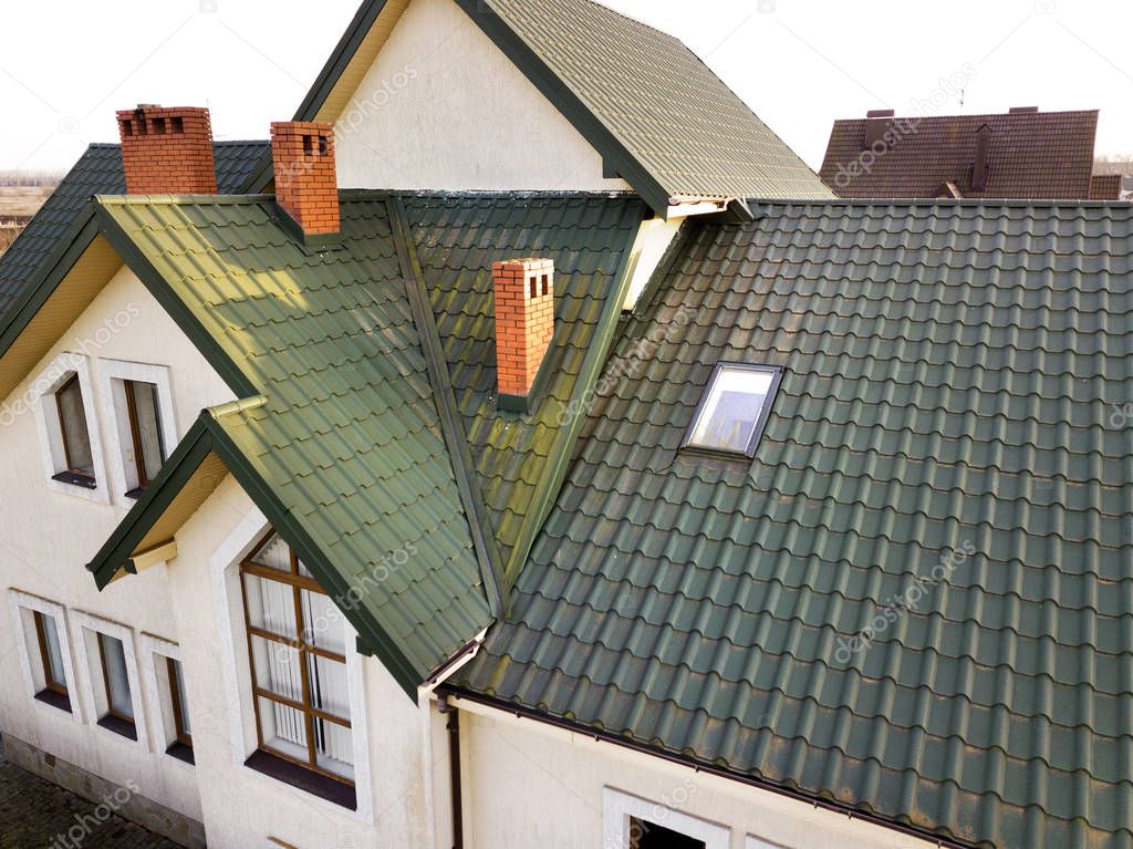Green metal shingled house roof with attic plastic window and br