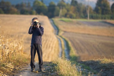 Elinde fotoğraf makinesi olan küçük çocuk buğday tarlasının fotoğrafını çekiyor. 