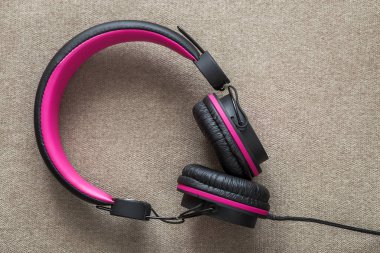 Headphone black and pink isolated on light cloth flat copy space background. Modern technology, trendy entertainment, gadget design and accessories concept.