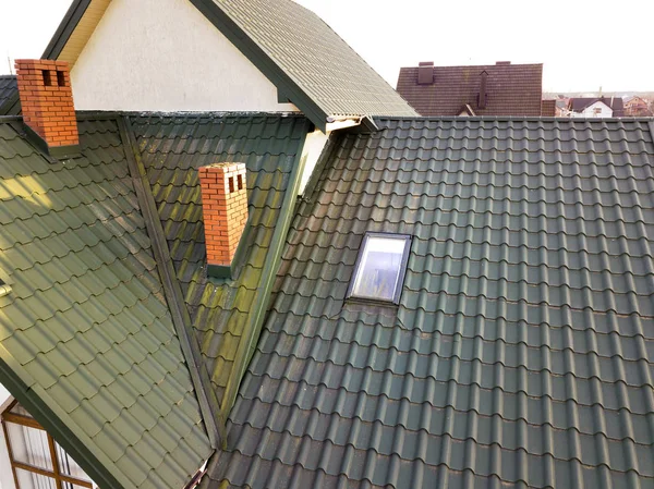 Green metal shingled house roof with attic plastic window and br