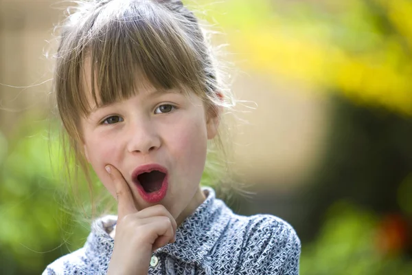 Niedliche hübsche Kind Mädchen mit lustigem Ausdruck im Freien auf verschwommenem sonnigen grün und gelb hellem Hintergrund. — Stockfoto