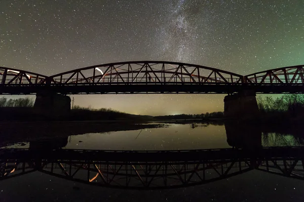 Ponte metálica iluminada sobre suportes de betão refletidos na água — Fotografia de Stock
