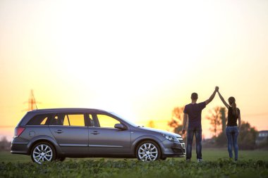 Genç çift, uzun at kuyruğu ve atletik adam tutarak ince çekici kadın yeşil alanında açık gökyüzü günbatımı veya gündoğumu kopya alan arka plan, gümüş renkli araba, silah kaldırdı..