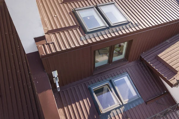 Widok z lotu ptaka na zewnątrz pomieszczenia z plastikowymi oknami poddasza, dach i ściany pokryte brązowym metalem dekoracyjnym deski boczniaków. — Zdjęcie stockowe