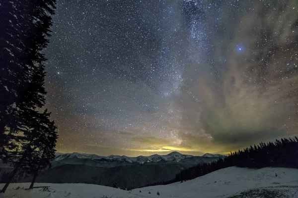 Mountain vinternatt Panorama efter solnedgången. Branta långa åsen bergstoppar, djup snö i dalen, kullar täckta med tät granskog, dramatiska snöiga stormiga moln på mörkblå stjärnhimmel. — Stockfoto